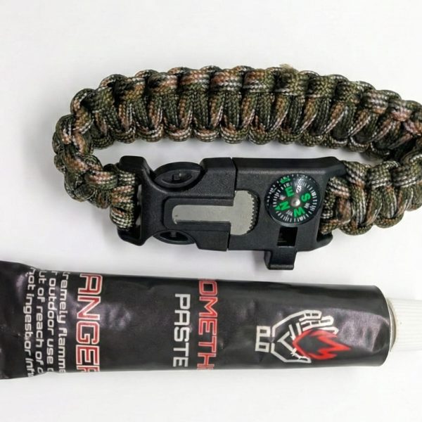 A green and black bracelet on a white surface with a compass clipped to it.