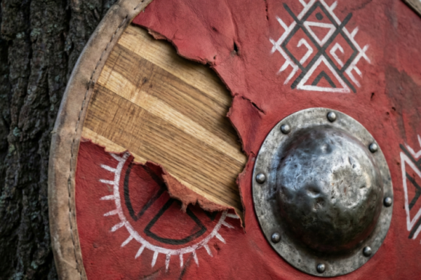 Large wooden shield with red and black designs in the forest.